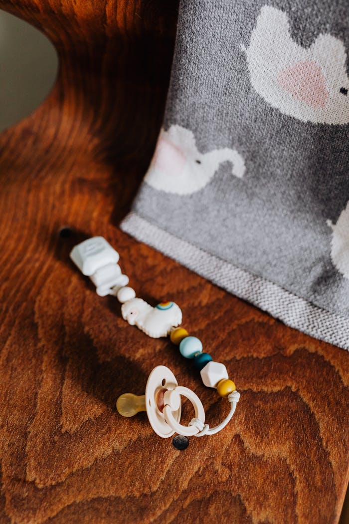 Close-up of a baby pacifier and beaded clip next to a grey blanket with elephants.